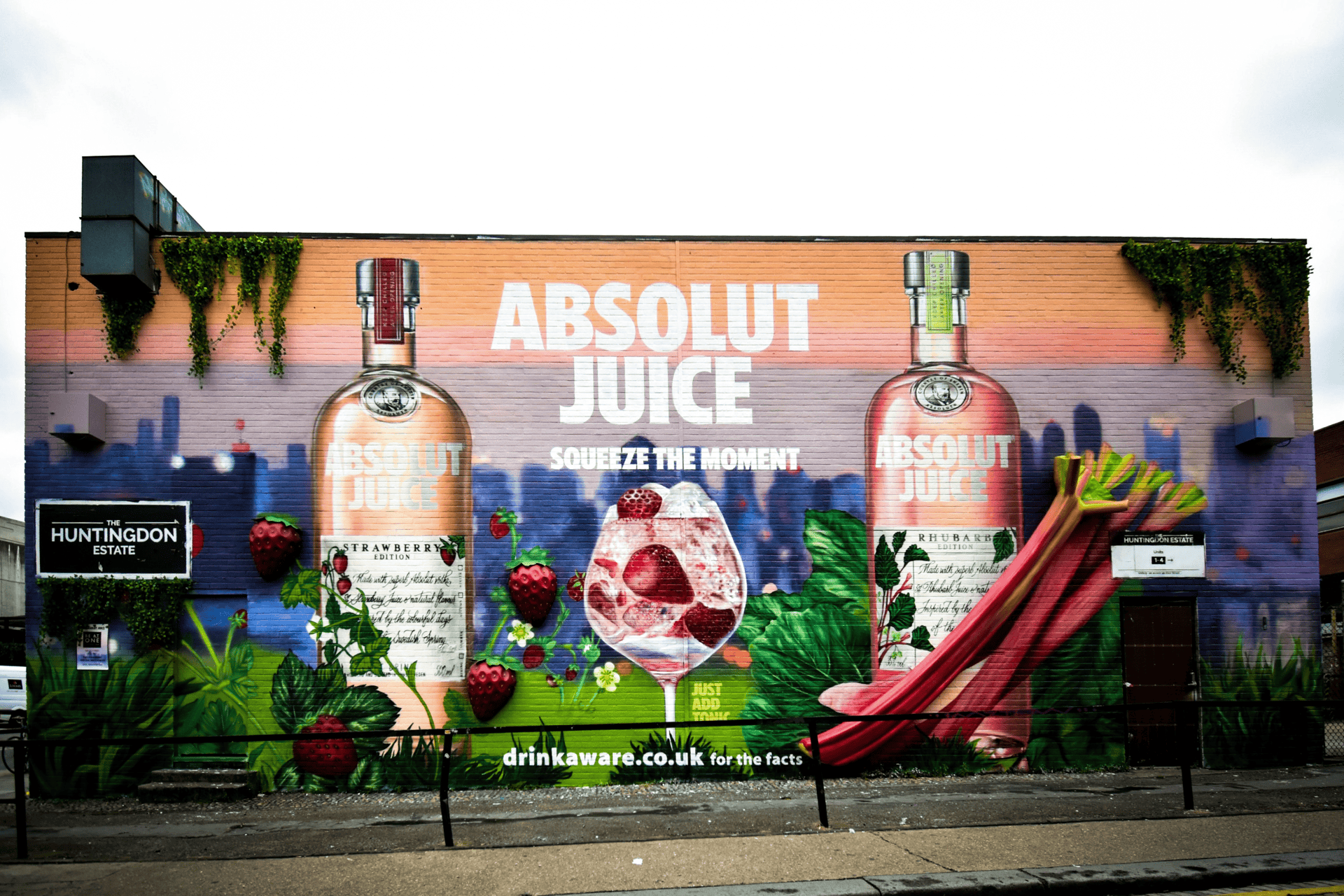 Mural of two Absolut Juice bottles with strawberries and rhubarb on a brick wall, colorful and vibrant, promoting 