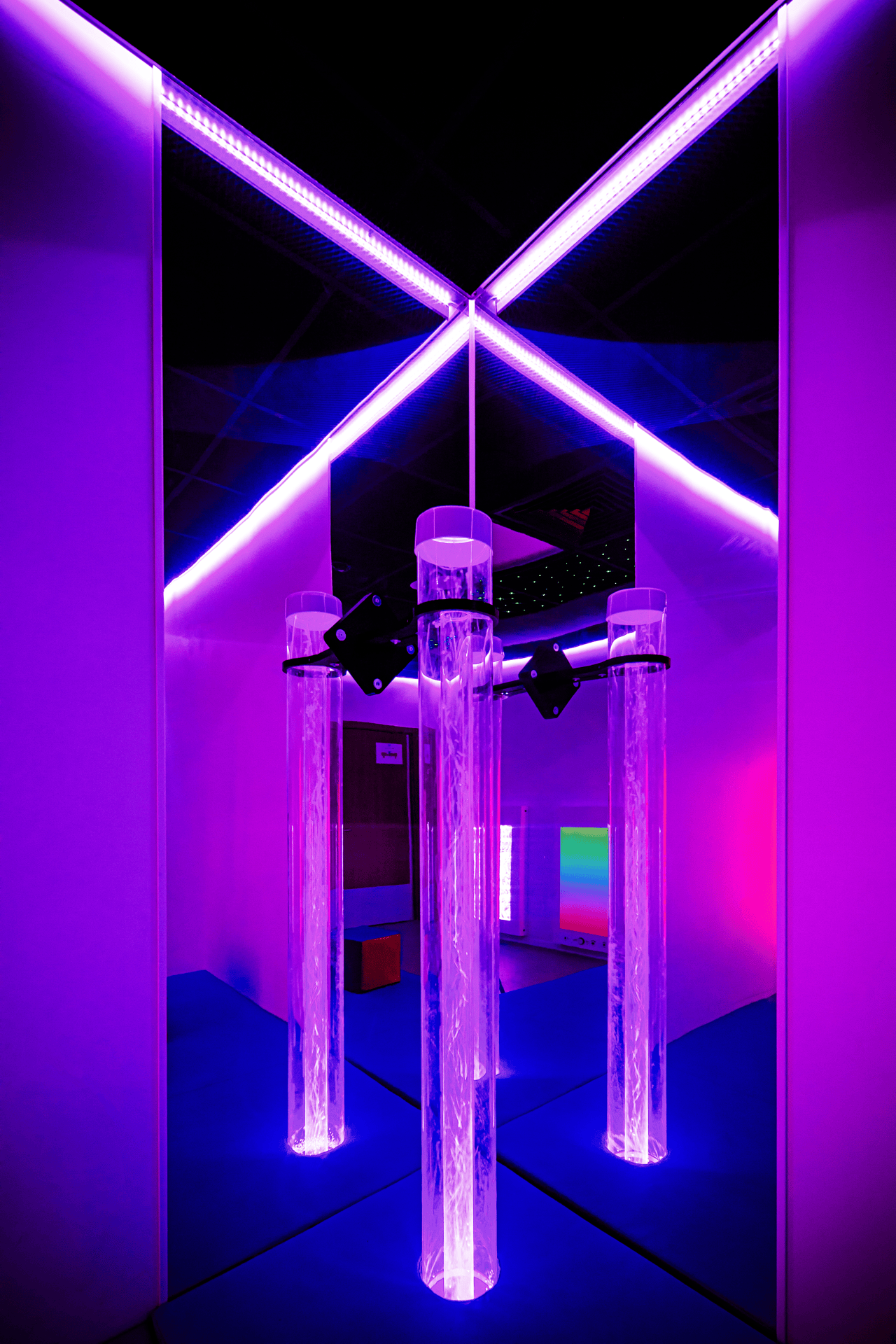 A room with bright purple lighting features three tall, illuminated acrylic tubes. The environment is futuristic and calming, evoking a sense of tranquility.