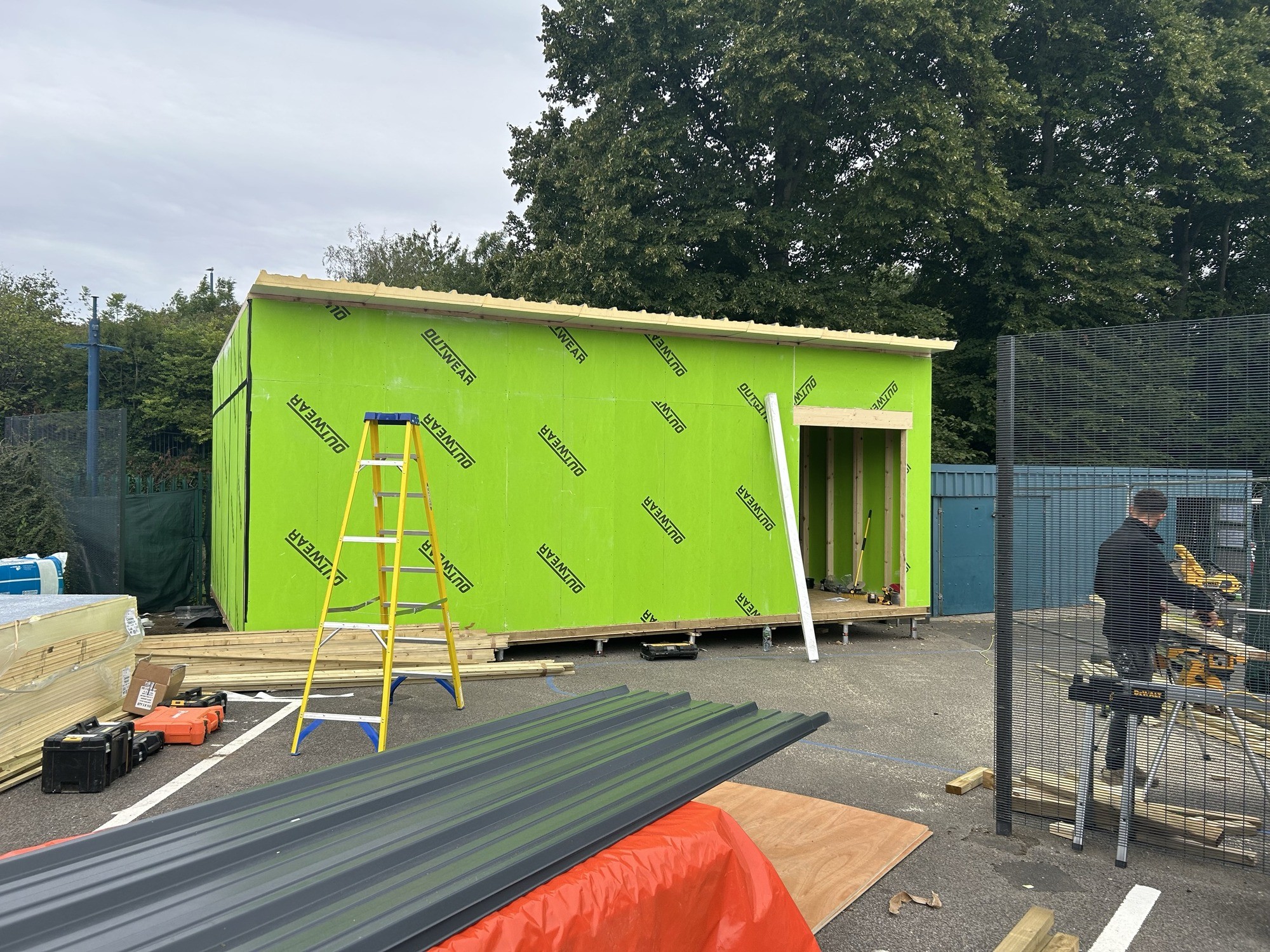 Construction of a wooden modular cabin with ladders and tools in the background.